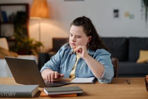 Ung kvinne med utviklingshemning sitter foran sin PC og ser konsentrert ut.