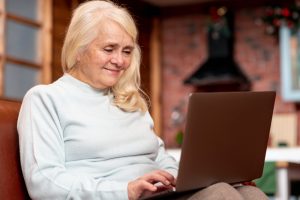 Smilende senior kvinne med PC i fanget.